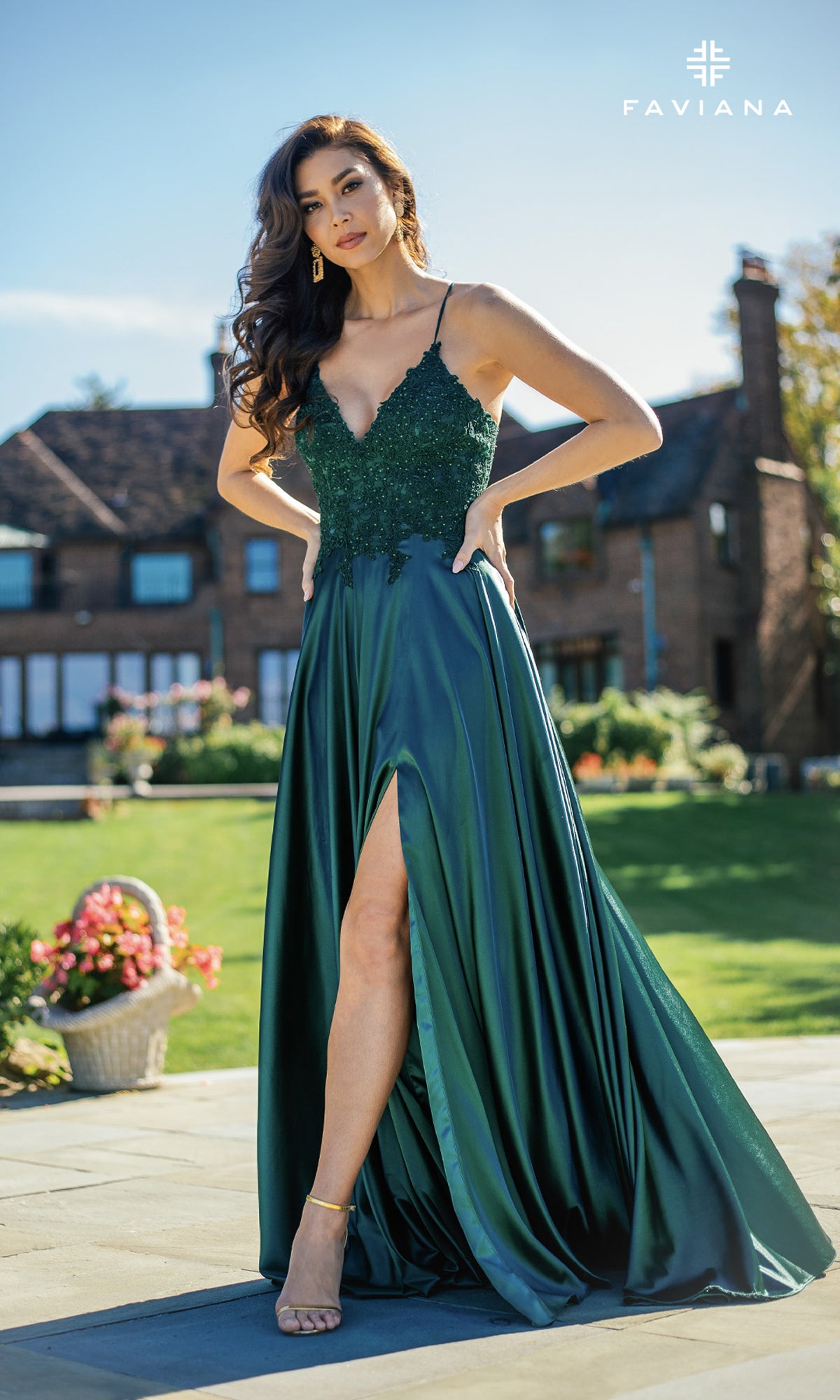 Woman outdoors on a patio in front of a brick house, wearing the Faviana Lace-Bodice Long A-Line Prom Dress—an elegant dark green, sleeveless gown with a thigh-high slit and delicate embroidered lace.